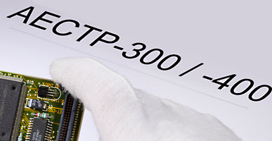 Auf einem Dokument steht AECTP-300 / -400 geschrieben, darüber ist der Ausschnitt einer Elektronikplatine zu sehen.