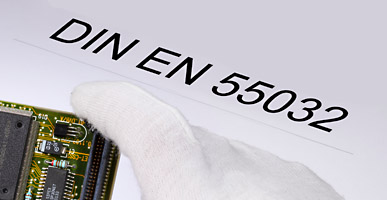 Auf einem Dokument steht DIN EN 55032 geschrieben, darüber ist der Ausschnitt einer Elektronikplatine zu sehen.