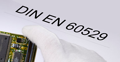 Auf einem Dokument steht DIN EN 60529 geschrieben, darüber ist der Ausschnitt einer Elektronikplatine zu sehen.