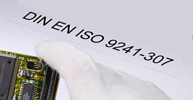 Auf einem Dokument steht DIN EN ISO 9241-307 geschrieben, darüber ist der Ausschnitt einer Elektronikplatine zu sehen.