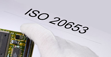 Auf einem Dokument steht ISO 20653 geschrieben, darüber ist der Ausschnitt einer Elektronikplatine zu sehen.