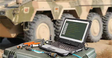 Laptop with tools on a box in front of a GTK BOXER wheeled armoured vehicle