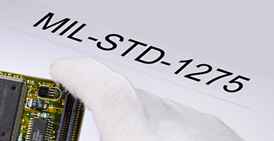 Auf einem Dokument steht MIL-STD-1275 geschrieben, darüber ist der Ausschnitt einer Elektronikplatine zu sehen.