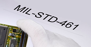 Auf einem Dokument steht MIL-STD-461 geschrieben, darüber ist der Ausschnitt einer Elektronikplatine zu sehen.