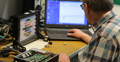 Electronics technician checking a device and looking at a computer monitor
